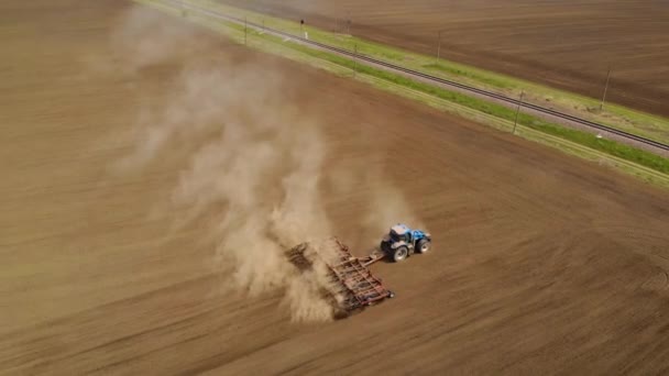 Luftaufnahme eines modernen blauen Traktors pflügt Feld mit Grubber vor der Aussaat und wendet am Rand der Ackerfläche — Stockvideo