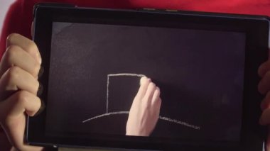 Kapalı kapılar ardında elinde tablet olan bir çocuk var. Kadın eli ağaçlı bir ev çiziyor.