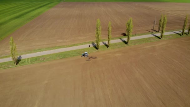 乾季に青いトラクターとディスクのハーローを持つフィールド間のアスファルト道路 — ストック動画