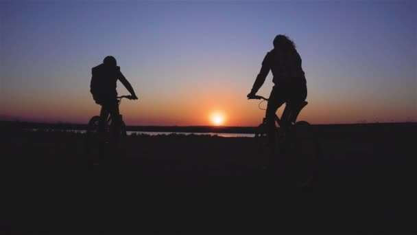 Dva cyklisté na horských kolech podél řeky v úžasných paprscích západu slunce — Stock video