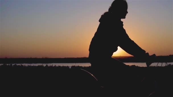 Повільний рух молодої жінки або дівчини, що їздить на велосипеді через річковий пляж і катається на вечірньому заході сонця. Красивий весняний настрій знімок волосся дме на вітер — стокове відео