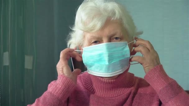 Portret van oude oma vrouw zetten op chirurgische masker voor corona virus preventie in haar kamer thuis — Stockvideo