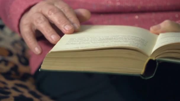 Mão de mulher velha virando páginas do livro ao lê-lo de perto. Luz cinematográfica em casa ou na biblioteca — Vídeo de Stock