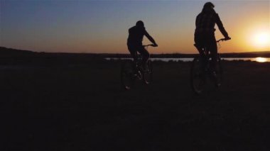 Anne ve oğlu gün batımında bisiklet sürerek şehir dışına çıkıyorlar. Retro biçimi yavaş çekim