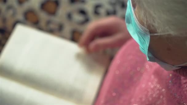 Old woman in protective face mask reading book at home during quarantine and self isolation — Stock Video