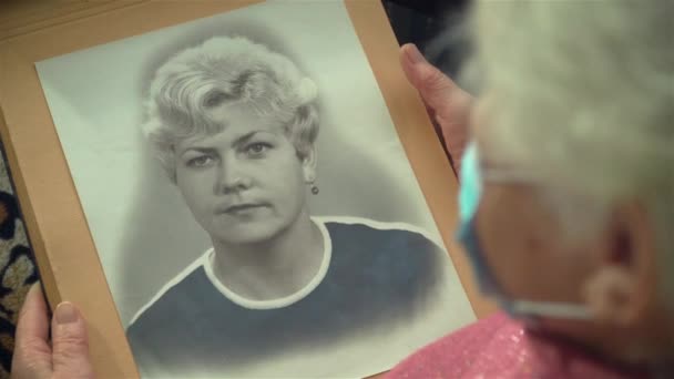 Alte Frau mit Schutzmaske betrachtet ihr Porträt auf dem Foto und erinnert sich an ihr junges Alter — Stockvideo