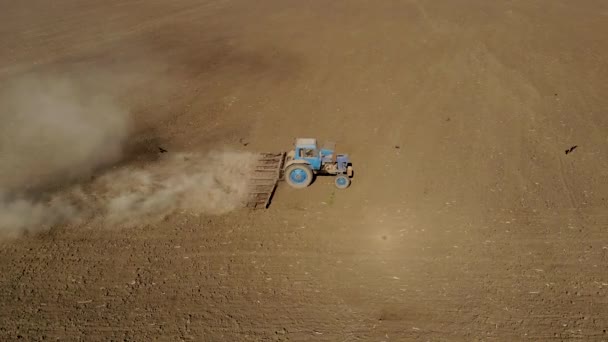 Exploitant aérien sur tracteur bleu labourant un sol aride poussiéreux. L'agro-industrie au printemps 