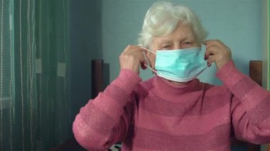 Evindeki odasında yüzüne koruyucu maske takmış yaşlı bir kadının portresi.