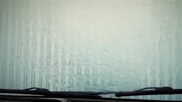 Wasser aus nächster Nähe an der Windschutzscheibe. Es regnet auf Glas. Auto in selbstreinigender Fahrzeugwaschanlage. Seifentropfen fließen Glas hinunter — Stockvideo