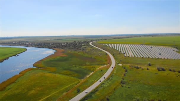Αεροφωτογραφία της μονάδας ηλιακών συλλεκτών παράγει ηλεκτρικό ρεύμα με τη βοήθεια του ηλιακού φωτός κοντά στο δρόμο με την οδήγηση αυτοκινήτων και του ποταμού — Αρχείο Βίντεο