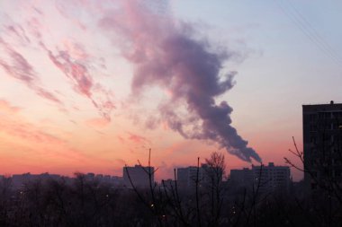 Pembe, mor, sarı ve mavi günbatımında bacadan dumanlar yükseliyor.