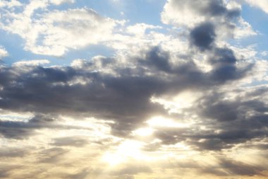 Güneşli, güzel bir gökyüzünün yatay fotoğrafı. Bulutların arkasından mavi ve sarı renkte güneş ışınları parlıyor.