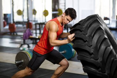 Yakışıklı kaslı adam spor salonunda büyük lastiği itiyor. Yatay kapalı çekim.