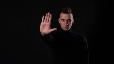 Siyah arka planda yakışıklı bir adam dur hareketi yapıyor..