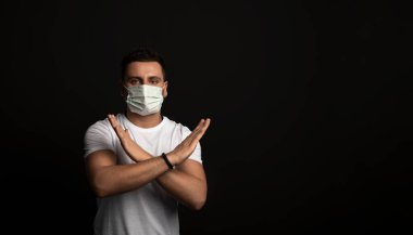 Siyah arka planda Asyalı bir adam, tıbbi maskeli bir adam iki kolunun çapraz olduğunu gösteriyor, işaret yok, dur işareti, virüsün duyguları, salgınlar, grip ve salgın hastalıklar, sis.