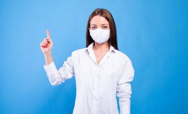 Beyaz önlüklü ve maskeli çekici bir kadın doktor portresi, bir parmağını göster..
