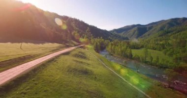 Güneşli yaz sabahında taze dağ nehri ve çayır üzerinde uçuşun ortasında. Aşağıdaki kırsal toprak yol
