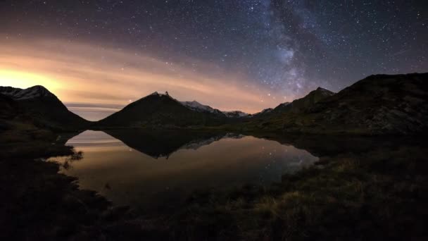 A aparente rotação da Via Láctea e o céu estrelado além da cordilheira coberta de neve refletiram-se no idílico lago apino. Orion Constellation vindo da esquerda no final. Tempo de lapso 4k vídeo . — Vídeo de Stock