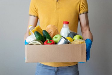 Eldivenli adam bir kutu yiyecek tutuyor. Bağış kutusunda yiyecek, konserve yiyecek, tahıl, sebze. Yemek teslimatı kavramı