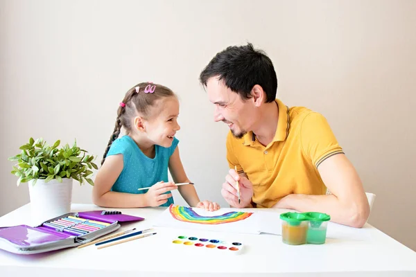 Baba ve kızı gülümser ve birlikte bir gökkuşağı çizerler. Baba ve çocuk ve iyi çizimler. Mutlu bir aile. Sevdiklerinle daha çok vakit geçir.