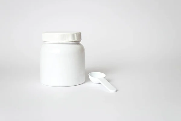 Beyaz plastik ilaç kavanozu ve beyaz arka planda ölçüm kaşığı.