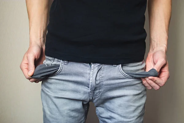 İş kaybı, düşük gelir, parasızlık kavramı. Kot pantolonlu ve siyah tişörtlü adam parasız cepleri gösteriyor.