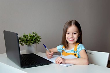 Eve çalışma mesafesi kavramı. Liseli kız dizüstü bilgisayarla masada oturuyor, ödev yapıyor ve gülümsüyor.