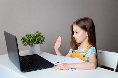 Evde eğitim. Eve çalışma mesafesi kavramı. Liseli kız dizüstü bilgisayarla masada oturuyor ve internetten iletişim kuruyor.