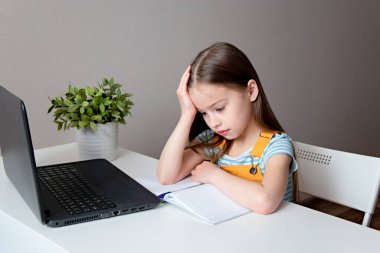 Evde eğitim. Eve çalışma mesafesi kavramı. Uzun saçlı liseli kız başını tutuyor. Yorgunluk hissi. Masada dizüstü bilgisayarla oturan üzgün kız.