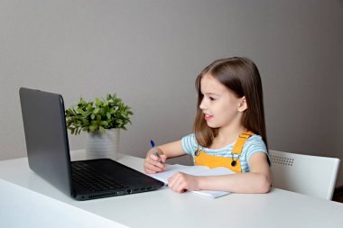 Evde eğitim. Eve çalışma mesafesi kavramı. Liseli kız dizüstü bilgisayarla masada oturuyor, ödev yapıyor.