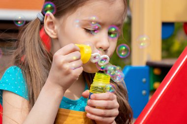 Güneşli bir günde, yaz mevsiminde oyun bahçesinde sabun köpüğü üfleyen çocuğu kapatın.