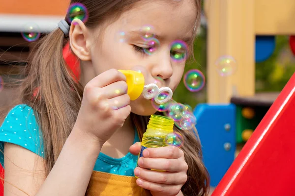 Güneşli bir günde, yaz mevsiminde oyun bahçesinde sabun köpüğü üfleyen çocuğu kapatın.