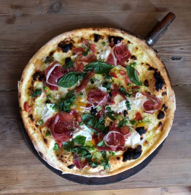 Klasik İtalyan pizzası, jambon, peynir ve fesleğen restoranda ahşap tahtada servis ediliyor. 