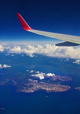 Uçan bir uçaktan görüş: uçak kanadı, gökyüzü, bulutlar, deniz ve adalar