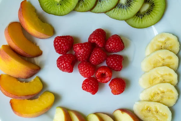 Buah segar. Pisang, kiwi, aprikot, raspberry, apel. Vitamin di piring putih — Stok Foto