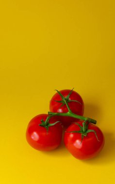 Sarı arka planda yeşil yapraklı üç domates. Üst görünümde dikey fotoğraf