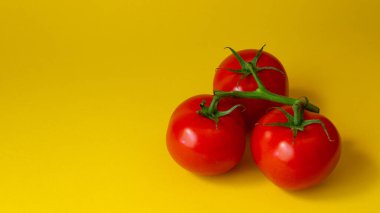 Sarı arka planda yeşil yapraklı üç domates. Fotoğrafı kapat. Yaz sebzeleri