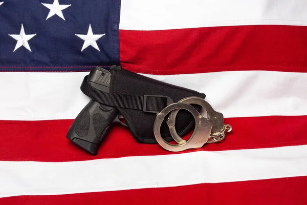 Gun, holster, and handcuffs in front of the American flag, horizontal