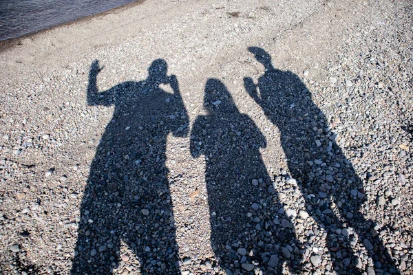 Three people taking shadow pics with their smart phones on the beach at Yellowstone Lake in Wyoming