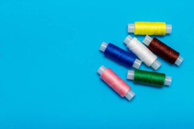 Mavi arka planda beyaz renkler, makas açık, ve turkuaz kurdele dikmek için, beyaz, mavi, yeşil, pembe, sarı iplik mavi arkaplanda, kopyalama alanı, üst görünüm