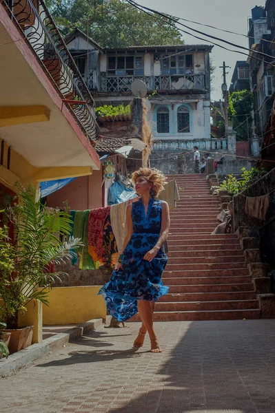 Eski Hint şehrinin arka planında, parlak mavi elbiseli güzel bir kız sokakta mutlu bir şekilde yürüyor.