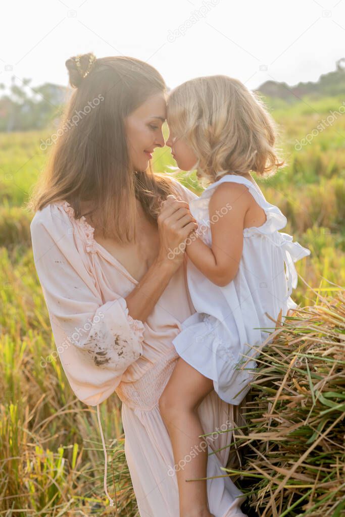 beautiful brunette mom with a tender blonde daughter in a mown field