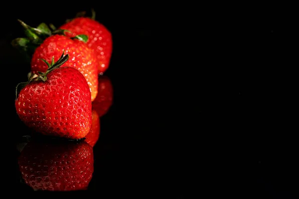 Três morangos maduros em um fundo preto com um reflexo com um espaço de cópia — Fotografia de Stock