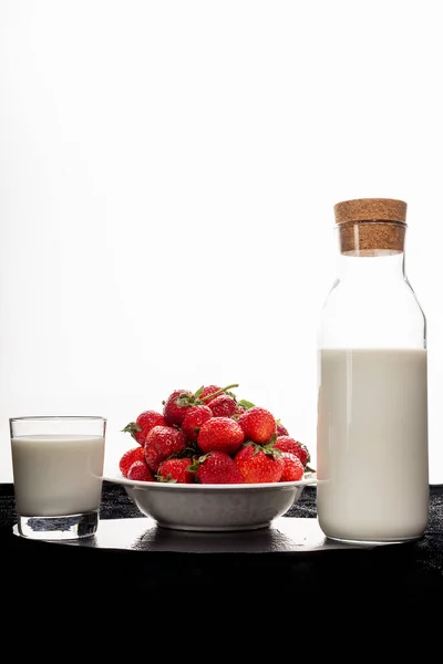 Uma garrafa de leite, um prato de morangos, um copo de leite em um pano preto em um fundo branco — Fotografia de Stock