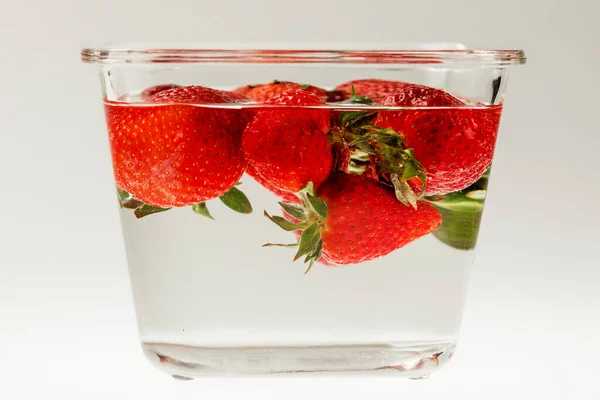 Beyaz arka planda cam bir kapta taze çilekler. Yan görünüm