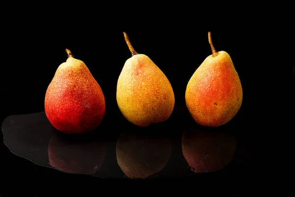 Siyah arka planda yansıması olan üç sarı-kırmızı armut.