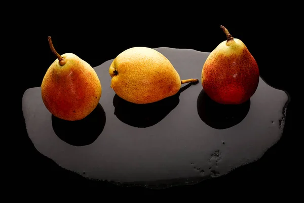 Siyah arka planda ıslak bir tepside üç olgun sarı armut.