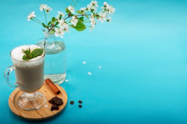Nane yaprağı ve çikolata parçalarıyla sabah kapuçinosu kiraz çiçeği filizinin yanındaki ahşap tezgahta..