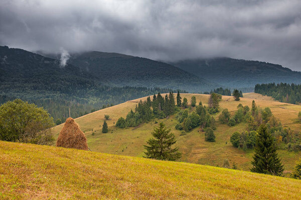 Haystack on mountain meadow with dramatic stormy sky. Ukraine, Europe