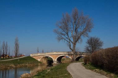 Eski taş köprü, Black River 'ın karşısına barok-sanat tarzında inşa edilmiş. Suyu kaplayan yol. Yüksek ağaçlar. Parlak mavi gökyüzü. Kralova pri Senci, Slovakya.